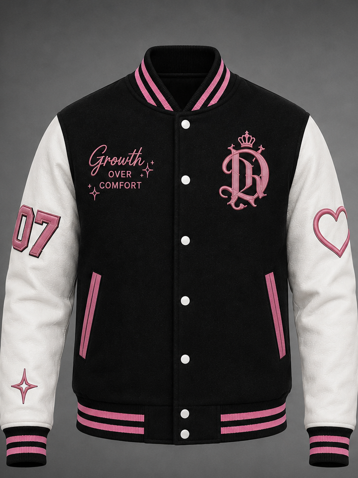 A varsity-style jacket with a black body and white sleeves, featuring pink striped ribbed collar, cuffs, and hem. The front has pink embroidered text reading 'Growth OVER COMFORT' on the right chest, a pink monogram crest with a crown on the left chest, and pink sleeve graphics including '07' on the left arm and a heart outline on the right arm.