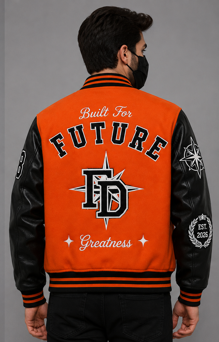 A man viewed from the back wearing a bright orange and black varsity-style jacket with large embroidered text reading 'Built For FUTURE Greatness' and a large 'FD' monogram on the back, against a plain gray studio background.