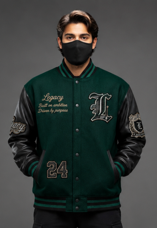 A man wearing a dark green varsity-style jacket with black leather sleeves, a black face mask, and a gray studio background. The jacket features embroidered details, including a large letter 'L' on the left chest, script text on the right chest, and the number '24' on the lower front.