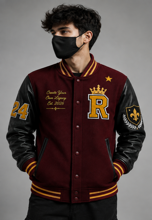 A man wearing a custom varsity jacket with a Maroon wool body, black leather sleeves, and gold and yellow trim. The jacket features a large gold letter 'R' with a crown, a fleur-de-lis patch on the sleeve, and custom text on the chest.