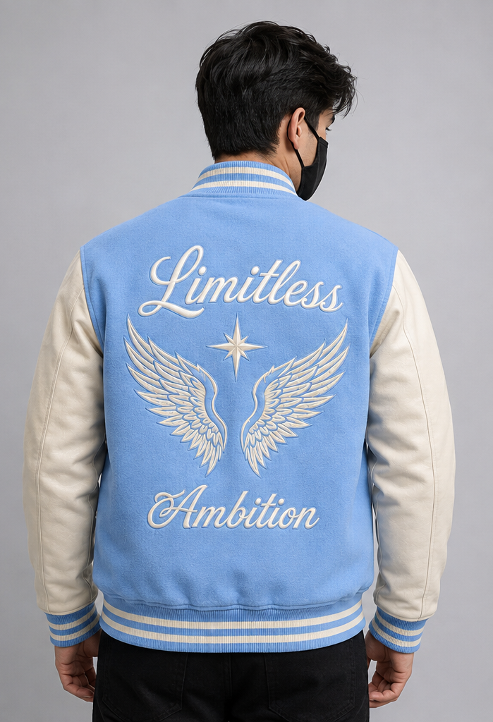 A man viewed from the back wearing a sky blue and white varsity jacket with 'Limitless Ambition' and angel wings embroidered on the back, set against a plain gray studio background.