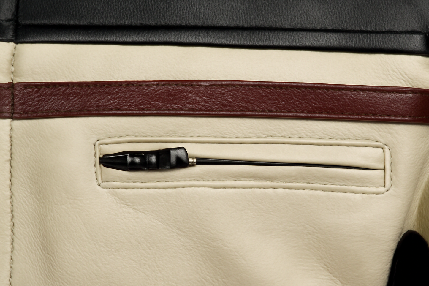 Close-up of a cream-colored leather pocket containing a black zip, with a dark brown leather horizontal stripe above it.