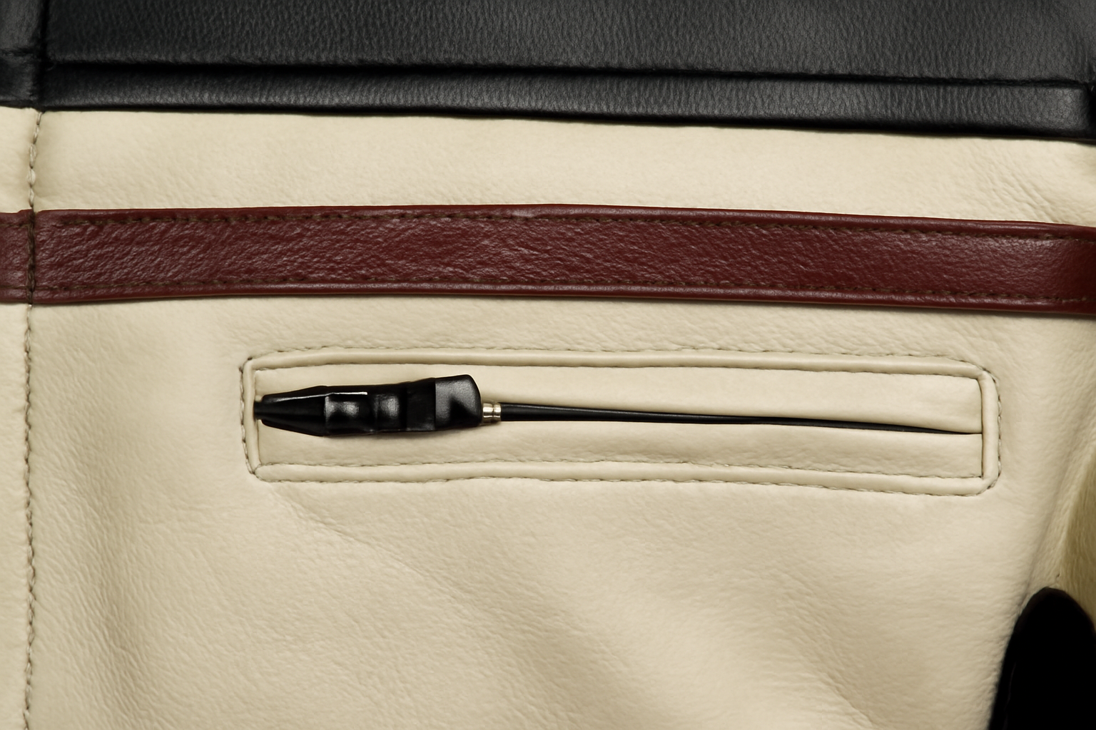 Close-up of a cream-colored leather pocket containing a black zip, with a dark brown leather horizontal stripe above it.