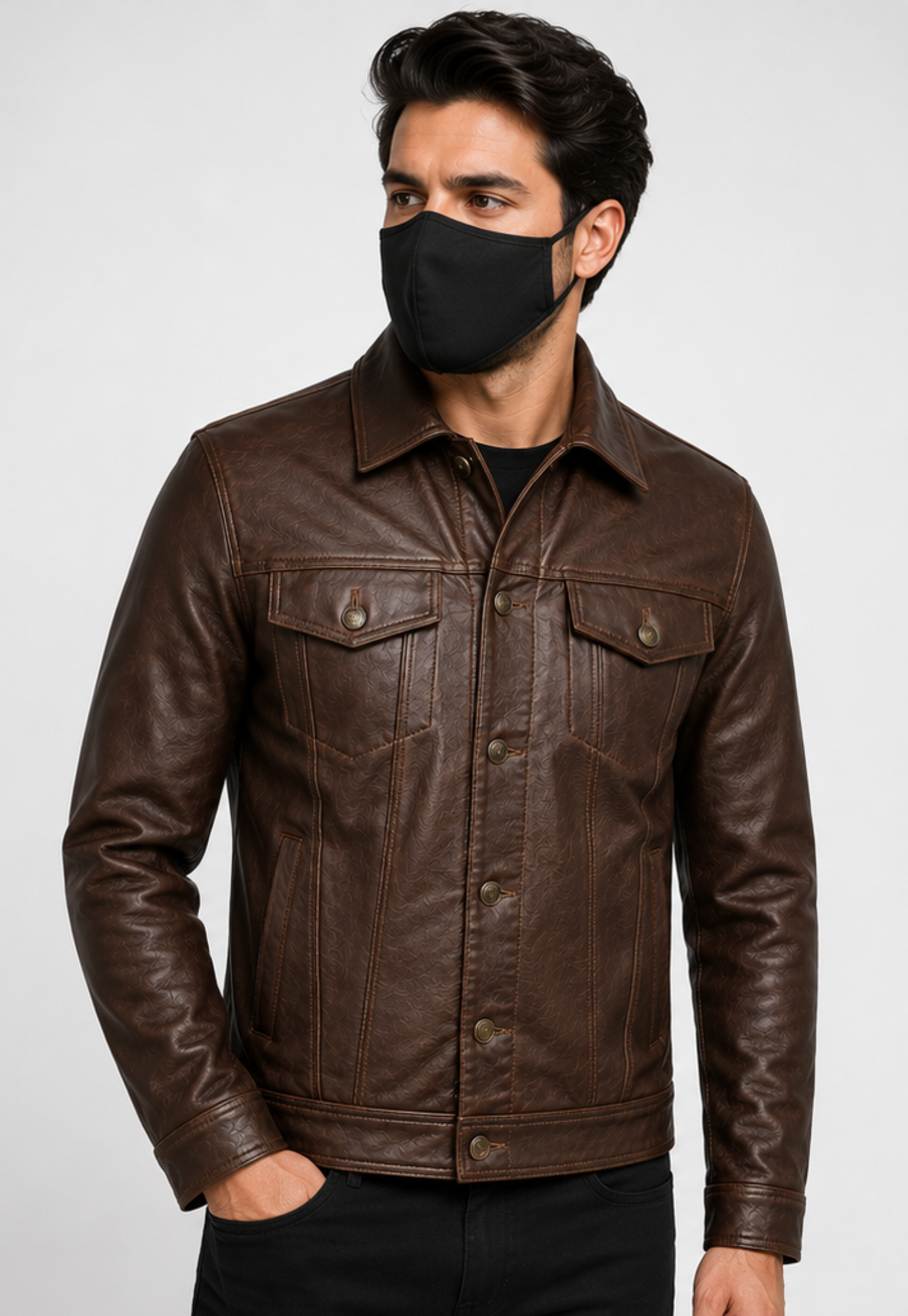 A man wearing a dark brown leather trucker jacket and a black face mask, photographed against a light gray studio background.