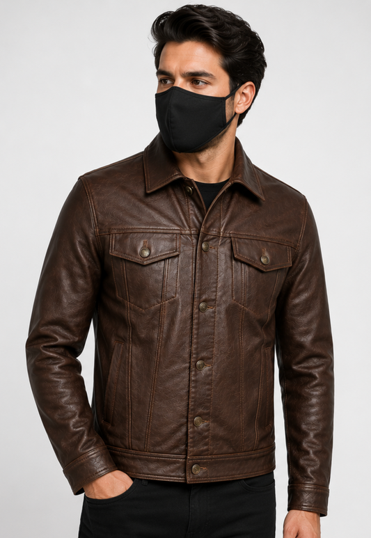 A man wearing a dark brown leather trucker jacket and a black face mask, photographed against a light gray studio background.