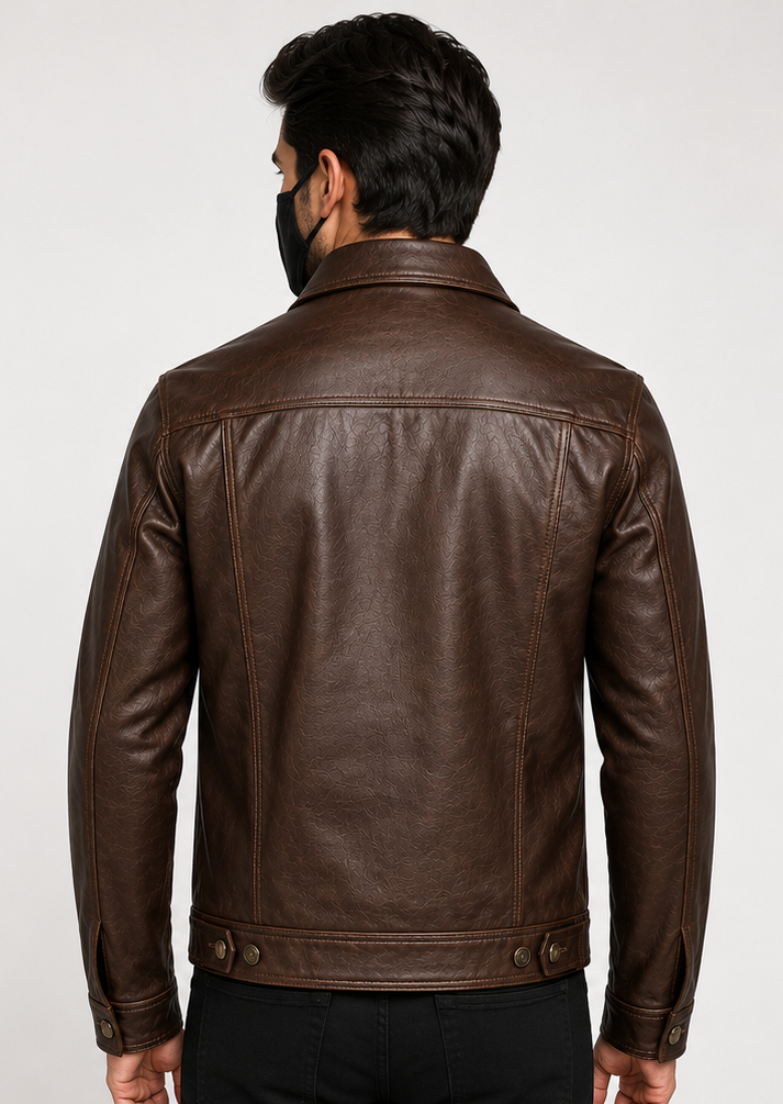 A man viewed from the back wearing a dark brown leather trucker jacket, black pants, and a black face mask, set against a plain light gray studio background.