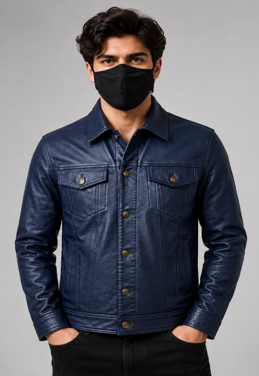 A man wearing a dark navy blue leather trucker jacket with brown buttons, paired with a black face mask and black pants, standing against a solid gray studio background.