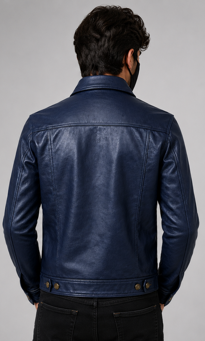 A man viewed from the back wearing a dark navy blue leather trucker jacket with a collar and button details at the waist, paired with black pants, against a neutral gray background.