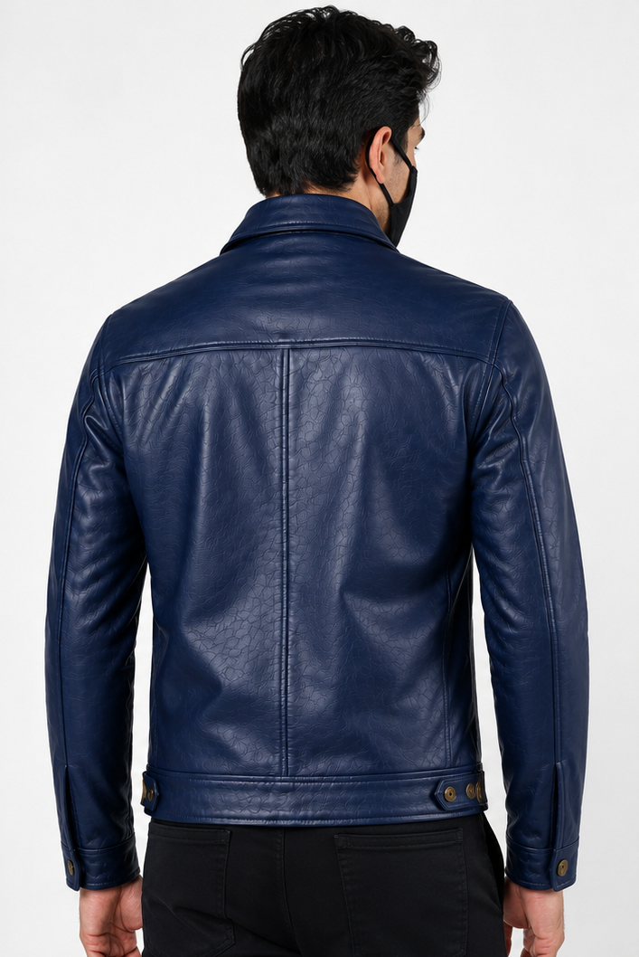 A man viewed from the back wearing a navy blue leather jacket, black pants, and a black face mask, against a plain light gray studio background.