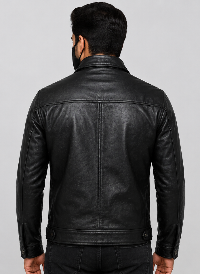 A man viewed from the back wearing a black leather jacket, black jeans, and a black face mask, set against a solid light gray studio background.