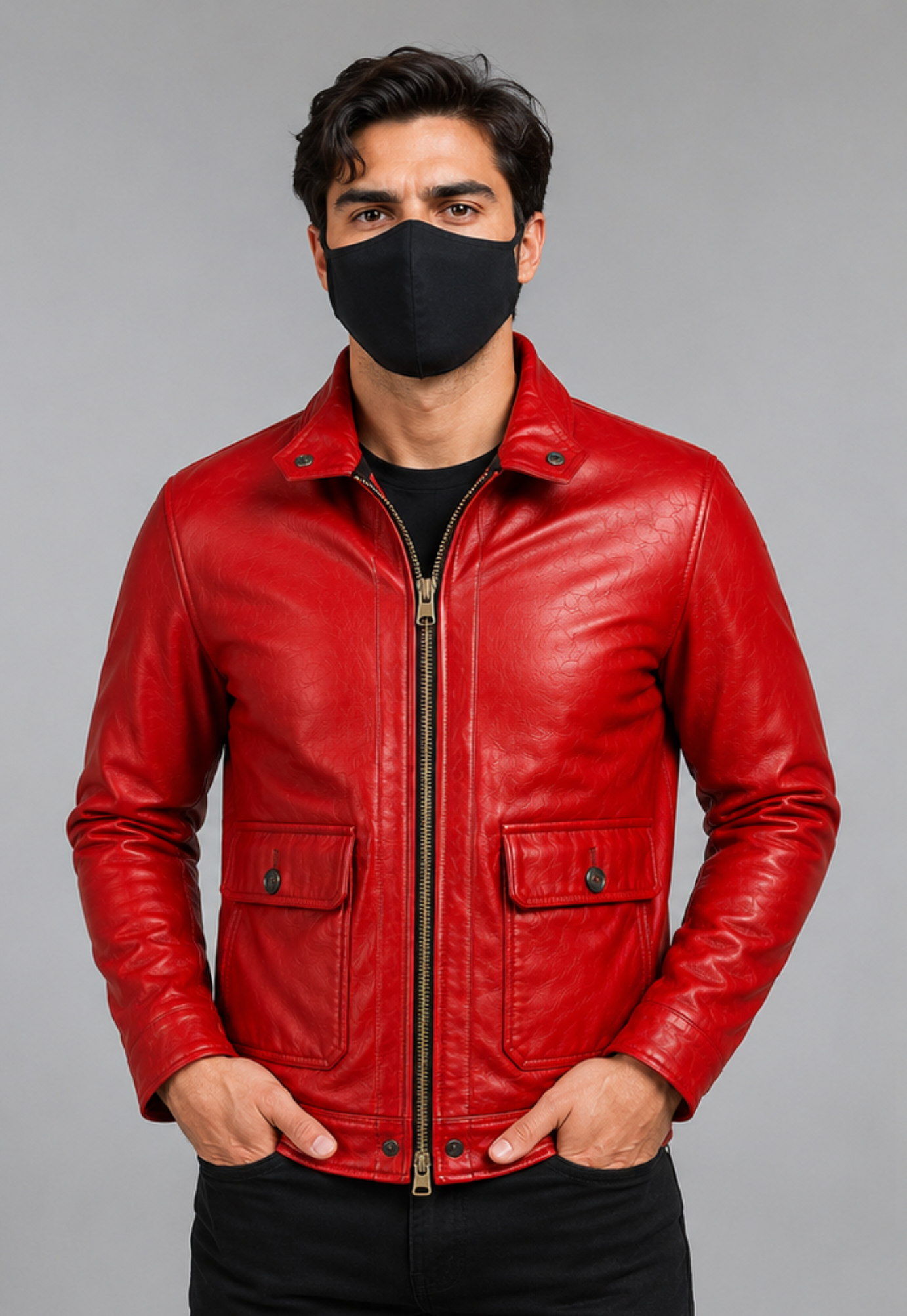 A man wearing a bright red leather jacket over a black shirt and black pants, with a black face mask, standing against a solid gray studio background.