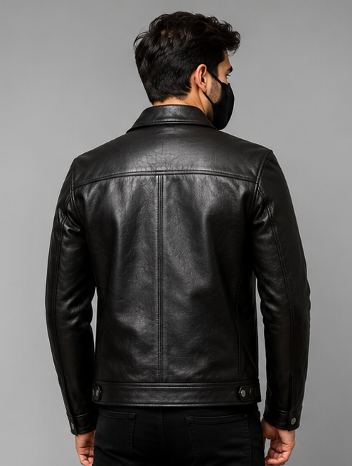 A man viewed from the back wearing a black leather jacket, black pants, and a black face mask, set against a solid gray studio background.