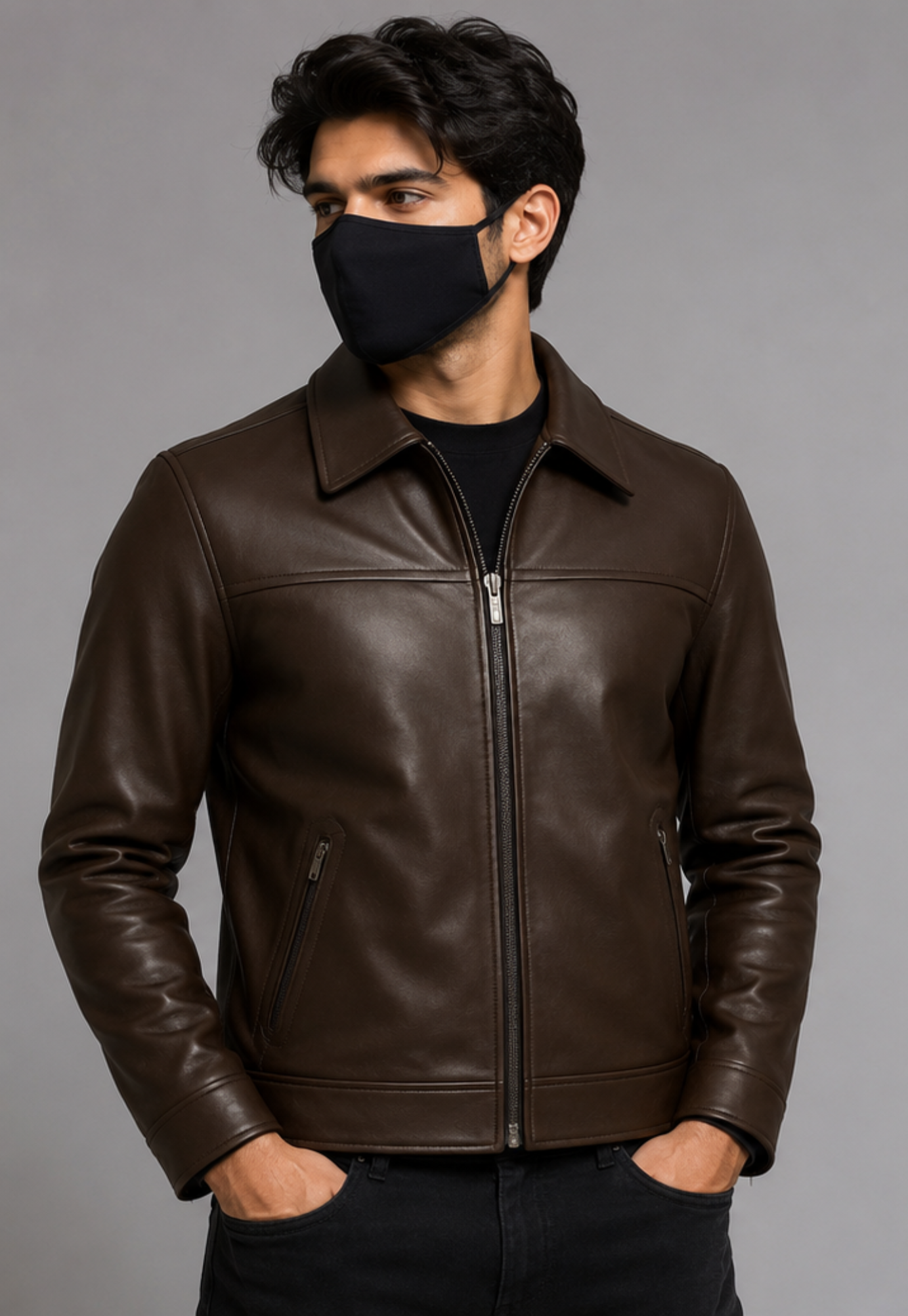 A man wearing a dark brown leather jacket with a black face mask, photographed against a plain gray studio background.