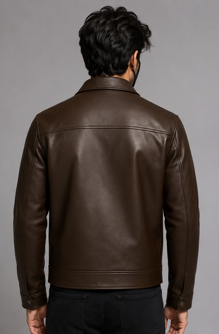 A man viewed from the back wearing a dark brown leather jacket and black pants, standing against a neutral gray studio background.