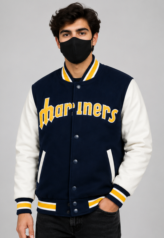A man wearing a navy and white varsity jacket with 'Mariners' written in yellow across the chest, paired with a black face mask, set against a plain gray studio background.