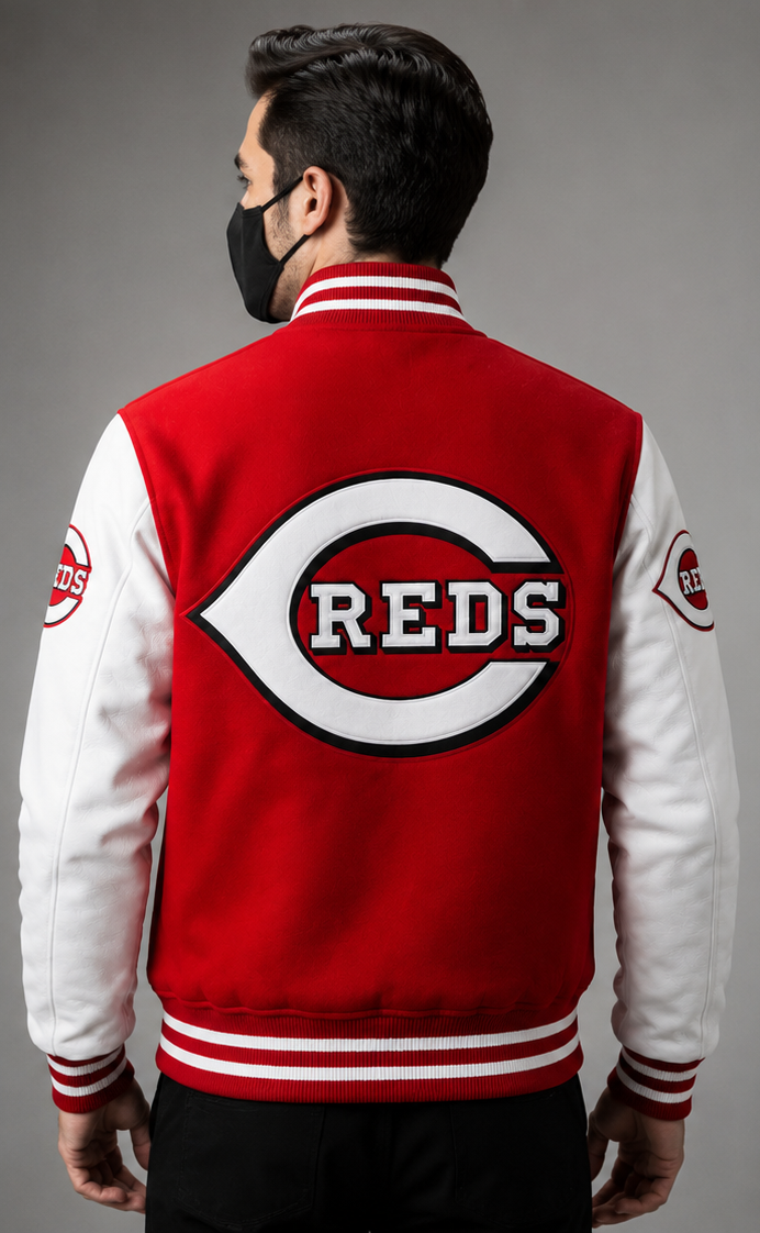 A man viewed from behind wearing a red and white varsity jacket with a large Cincinnati Reds 'C' logo on the back, set against a solid gray studio background.