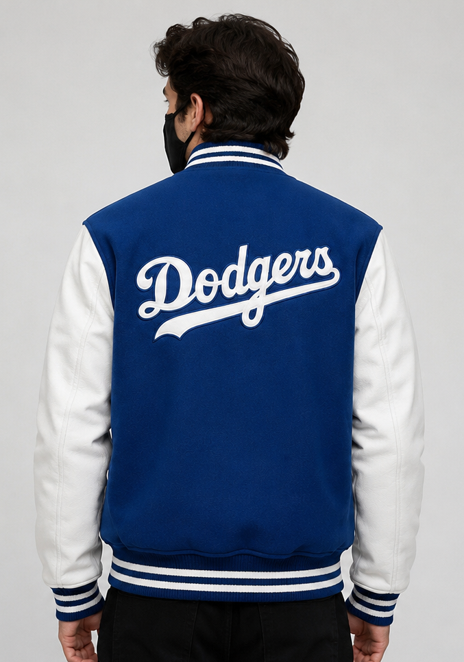 A man viewed from behind wearing a blue and white varsity jacket with 'Dodgers' embroidered in white script across the back, set against a plain light gray background.