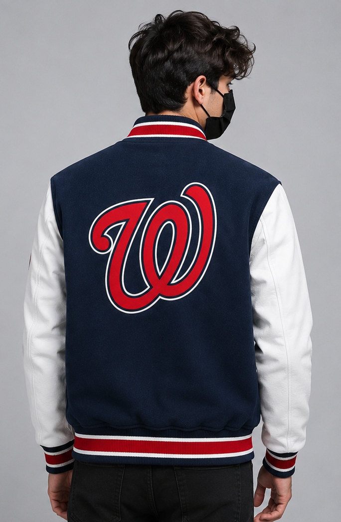 A man viewed from behind wearing a navy blue and white varsity jacket with a large red and white 'W' logo on the back, set against a solid gray studio background.