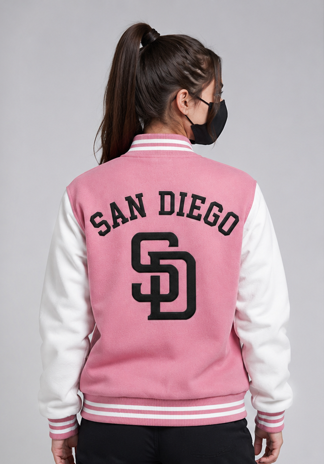A woman shown from the back wearing a pink and white varsity jacket with 'SAN DIEGO' and the 'SD' logo embroidered on the back, set against a plain gray studio background.