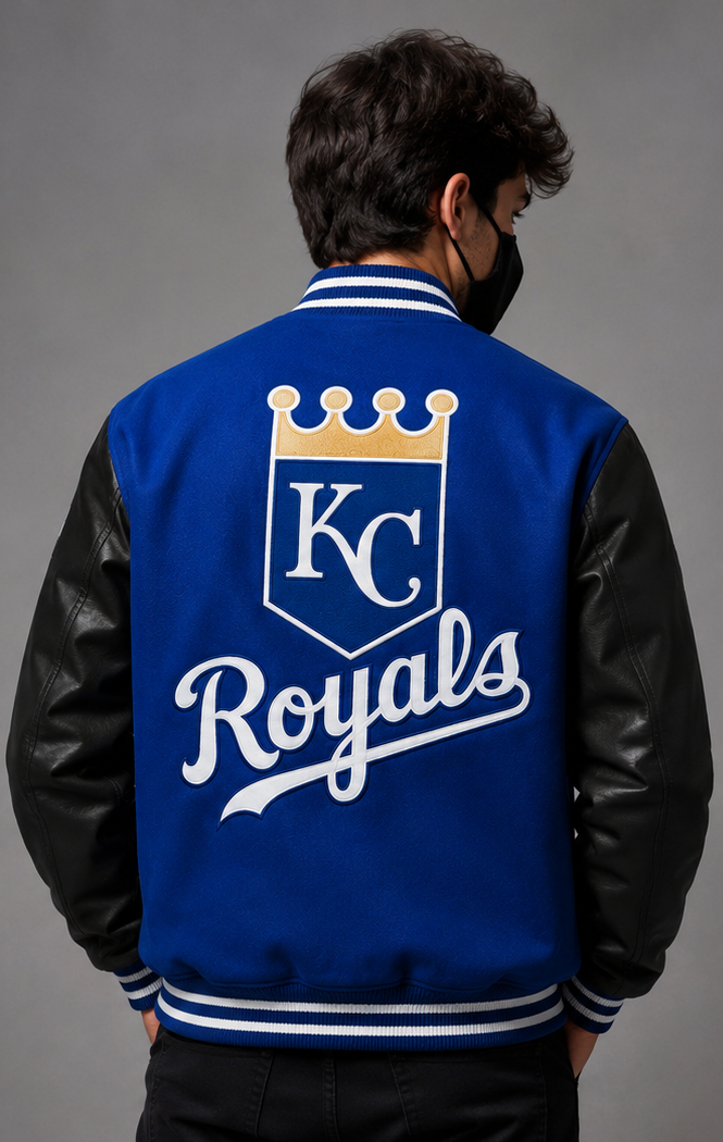 A man viewed from behind wearing a blue and black varsity jacket with the Kansas City Royals 'KC Royals' logo printed on the back. The jacket features a royal blue body, black leather-look sleeves, and white and blue striped ribbed collar, cuffs, and hem.