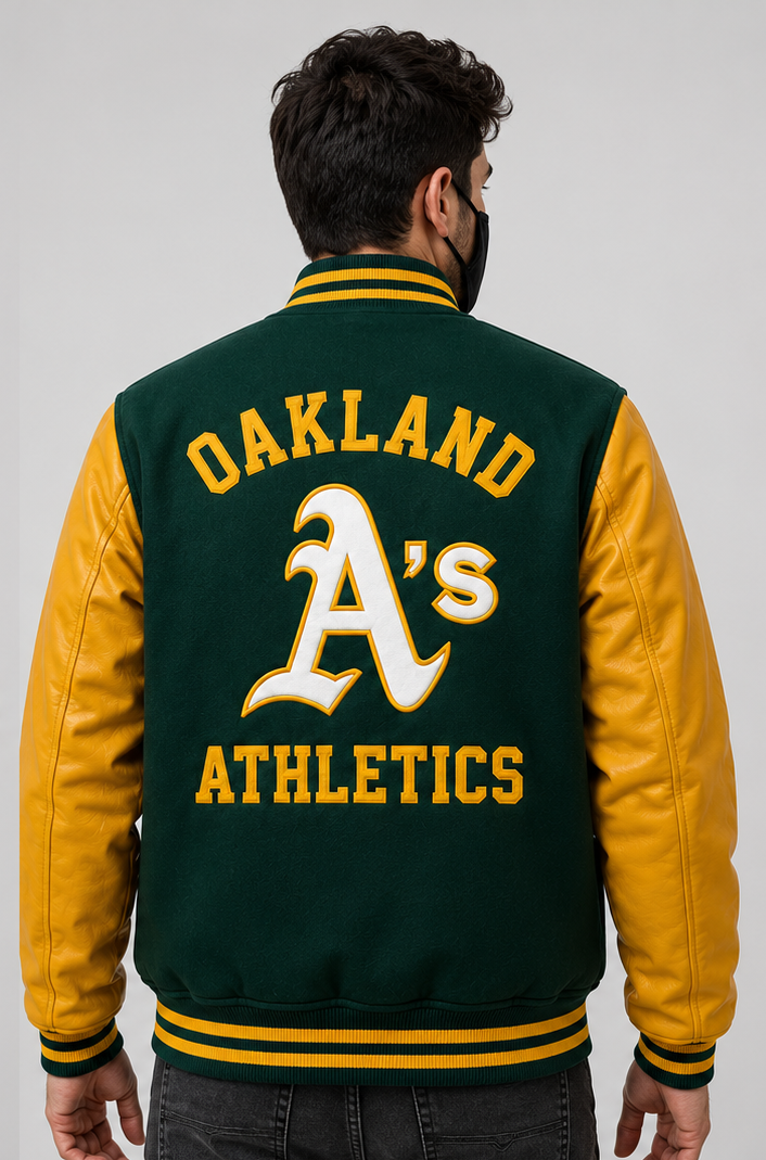 A man viewed from the back wearing a green and gold Oakland Athletics varsity jacket with 'OAKLAND A's ATHLETICS' embroidered on the back, set against a plain light gray background.