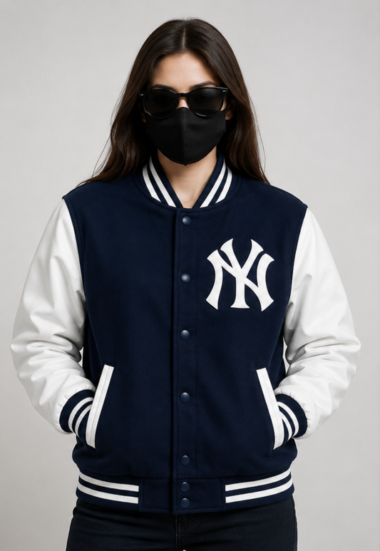 A woman modeling a navy and white varsity jacket with the New York Yankees logo on the chest, styled with a black face mask and sunglasses against a neutral gray background.