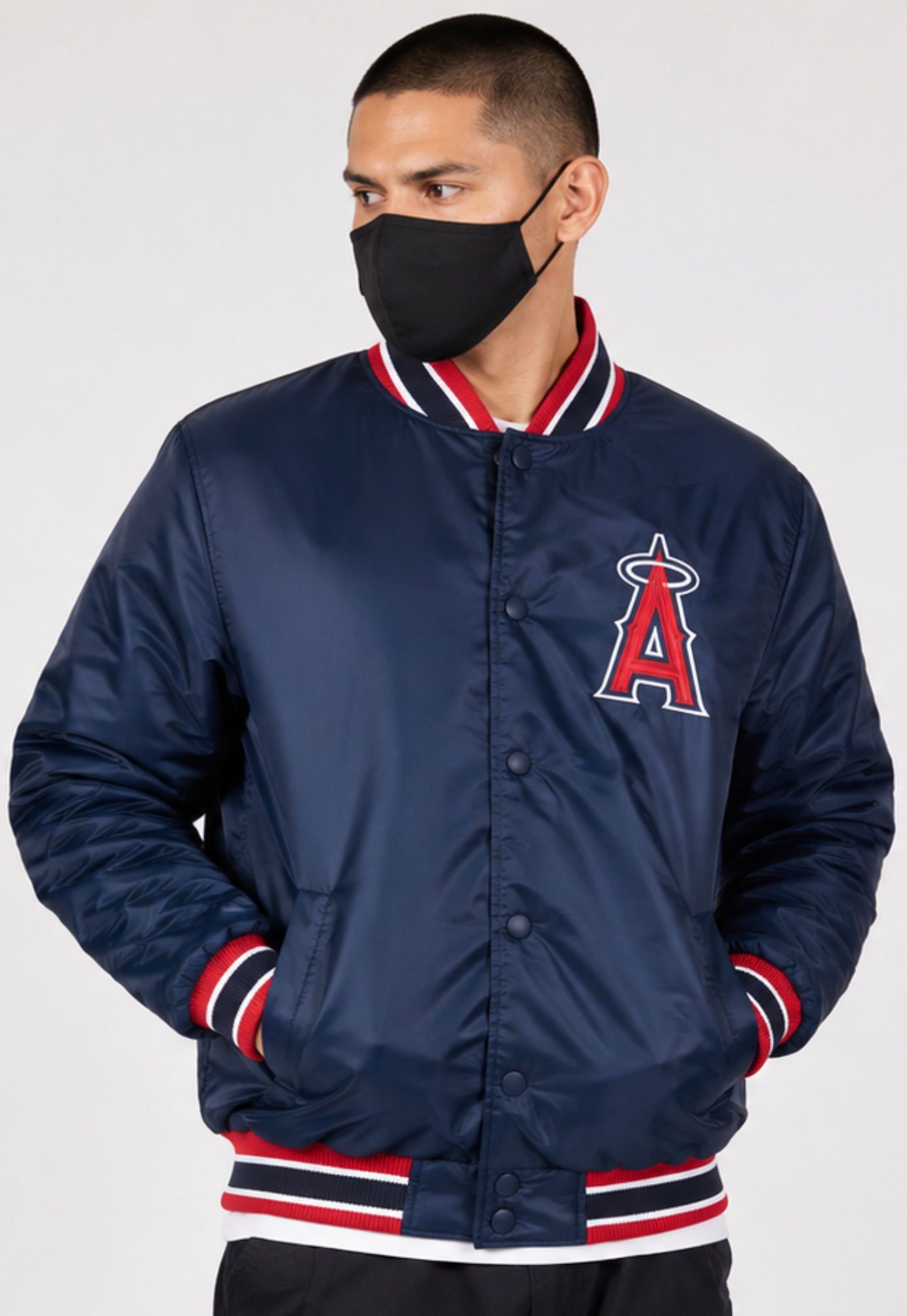 A man wearing a navy blue Los Angeles Angels varsity jacket with red and white striped ribbed collar, cuffs, and hem, paired with a black face mask, against a light gray studio background.