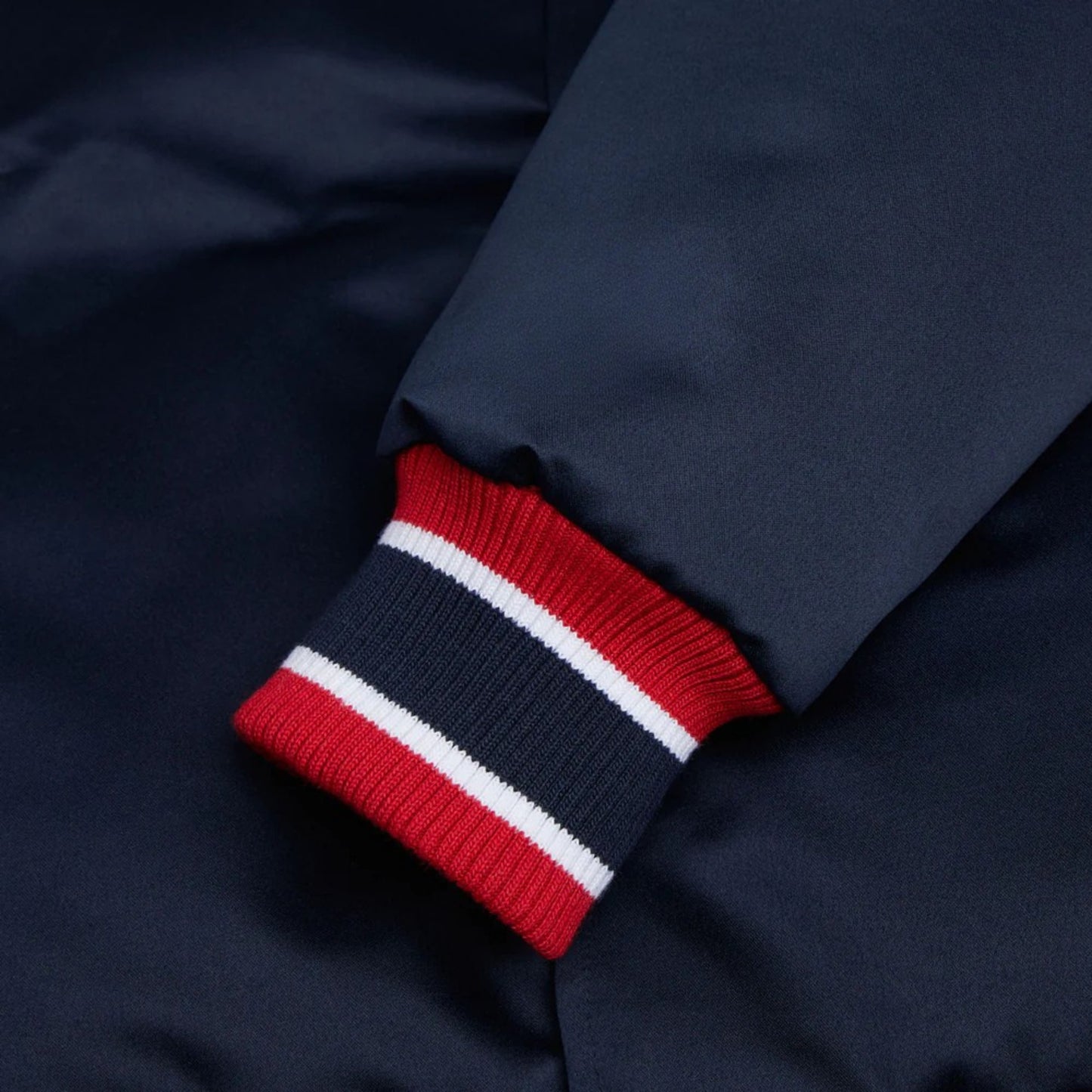 Close-up of a navy blue jacket with a red, white, and blue striped sleeve cuff.