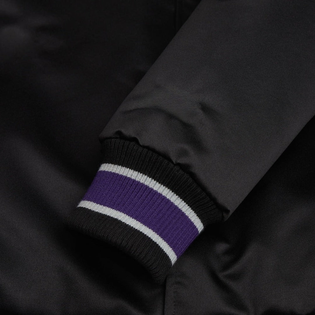 Close-up of a black jacket sleeve with purple and white striped cuffs.