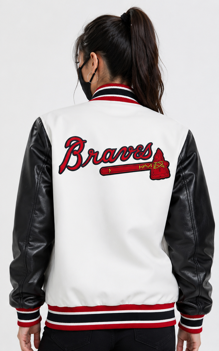 A woman viewed from the back wearing a white varsity-style jacket with black faux-leather sleeves and red, black, and white striped ribbing. The back features a large embroidered Atlanta Braves logo with an axe.