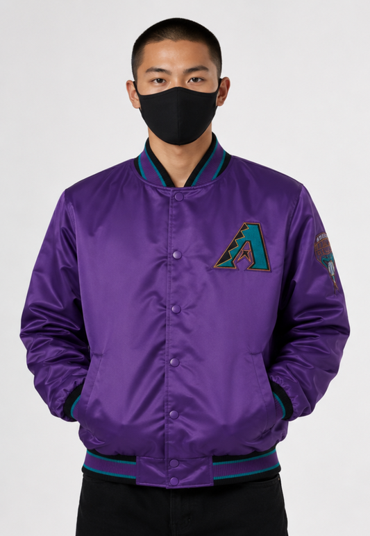 A man wearing a purple satin bomber jacket with a teal and black Arizona Diamondbacks 'A' logo on the chest, paired with a black face mask and black pants, against a light gray background.