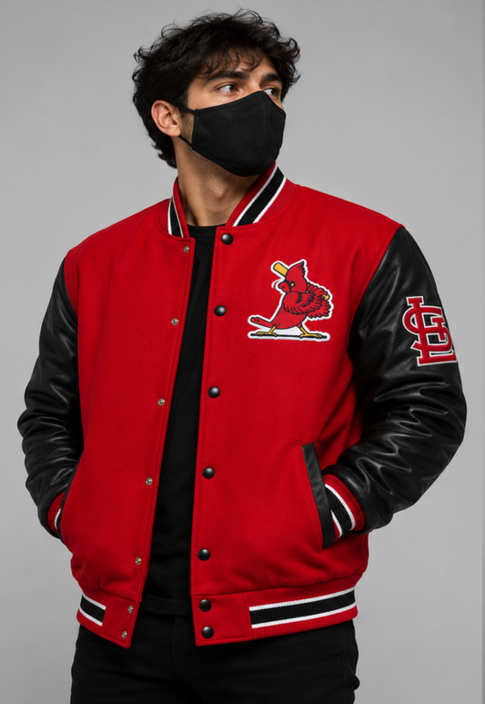 A man wearing a red and black varsity jacket with a St. Louis Cardinals logo on the chest, paired with a black face mask and black shirt, against a solid gray background.