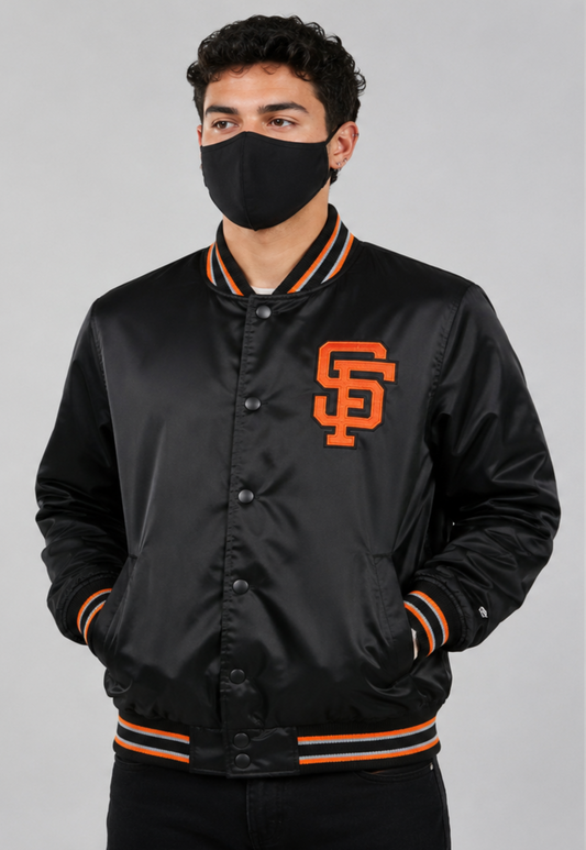 A man wearing a black satin varsity jacket with orange and white striped ribbing and a large orange 'SF' logo on the chest, paired with a black face mask, against a solid gray studio background.