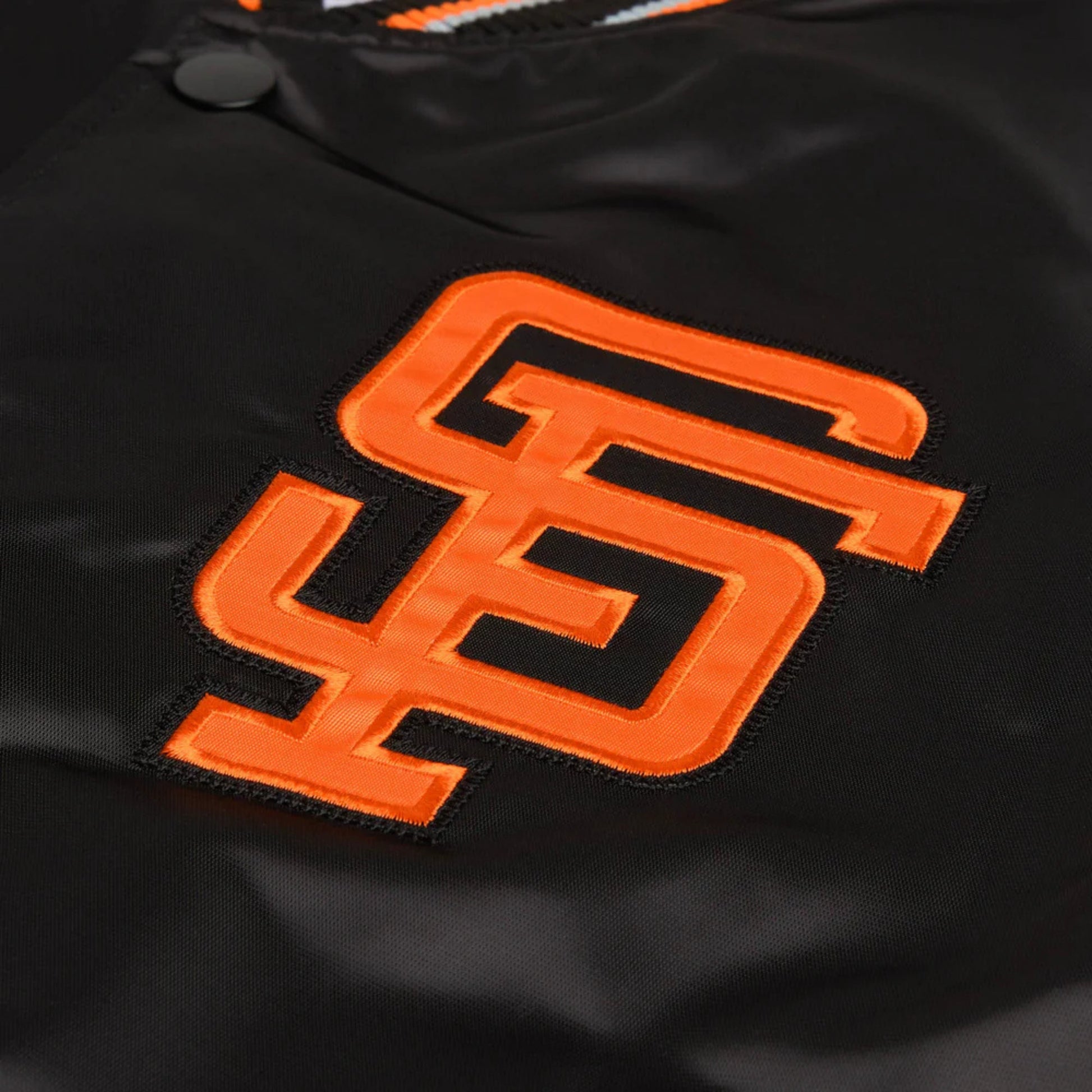 Close-up of a black satin or nylon jacket with a large orange embroidered San Francisco Giants 'SF' logo on the chest.
