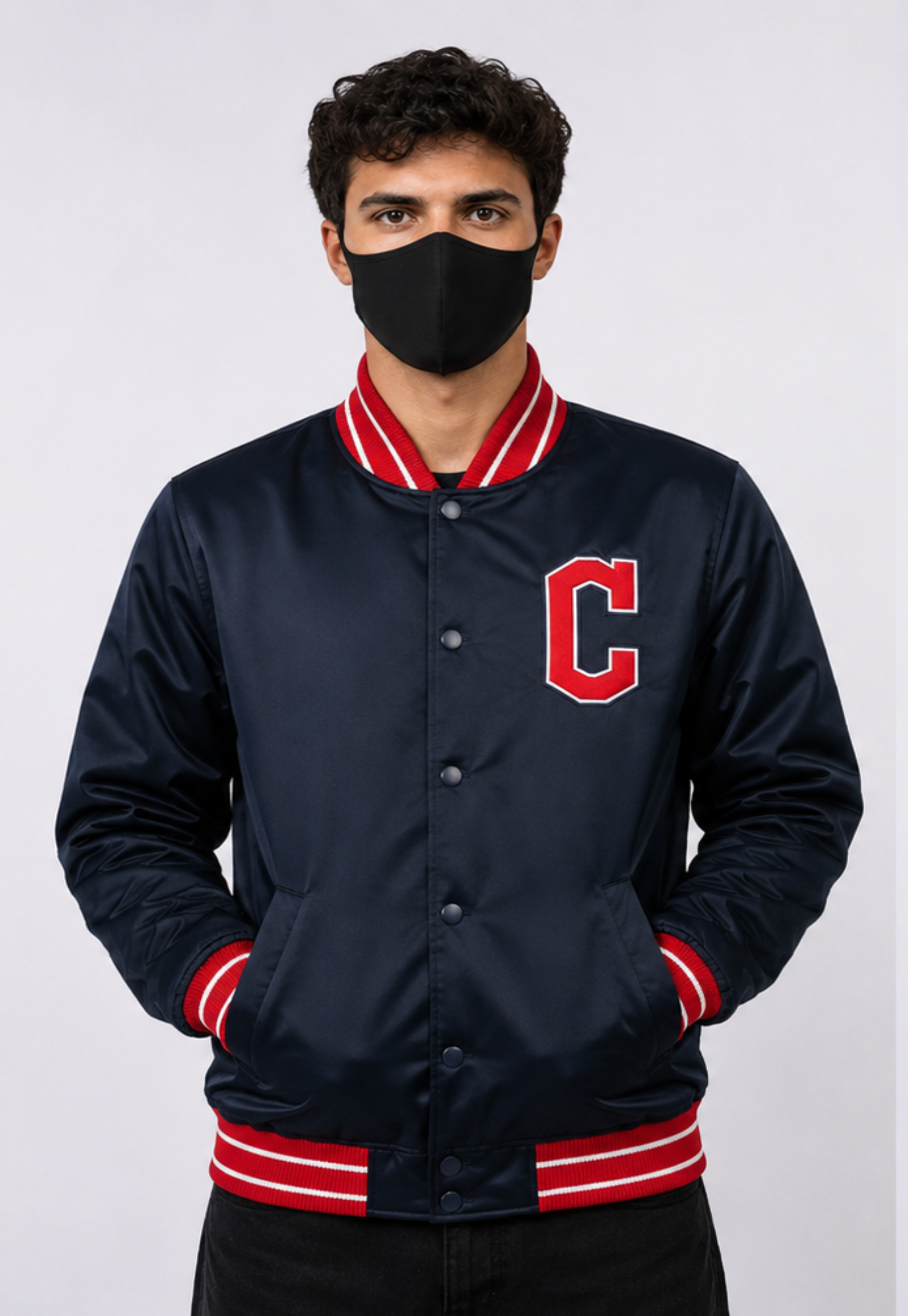 A man wearing a navy blue satin varsity jacket with red and white striped ribbed collar, cuffs, and hem, featuring a red letter 'C' on the chest. He is also wearing a black face mask, photographed against a light gray studio background.