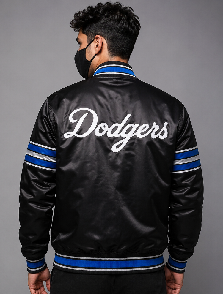 A man viewed from the back wearing a black satin Los Angeles Dodgers bomber jacket with white 'Dodgers' script on the back and blue and white striped ribbed trim.