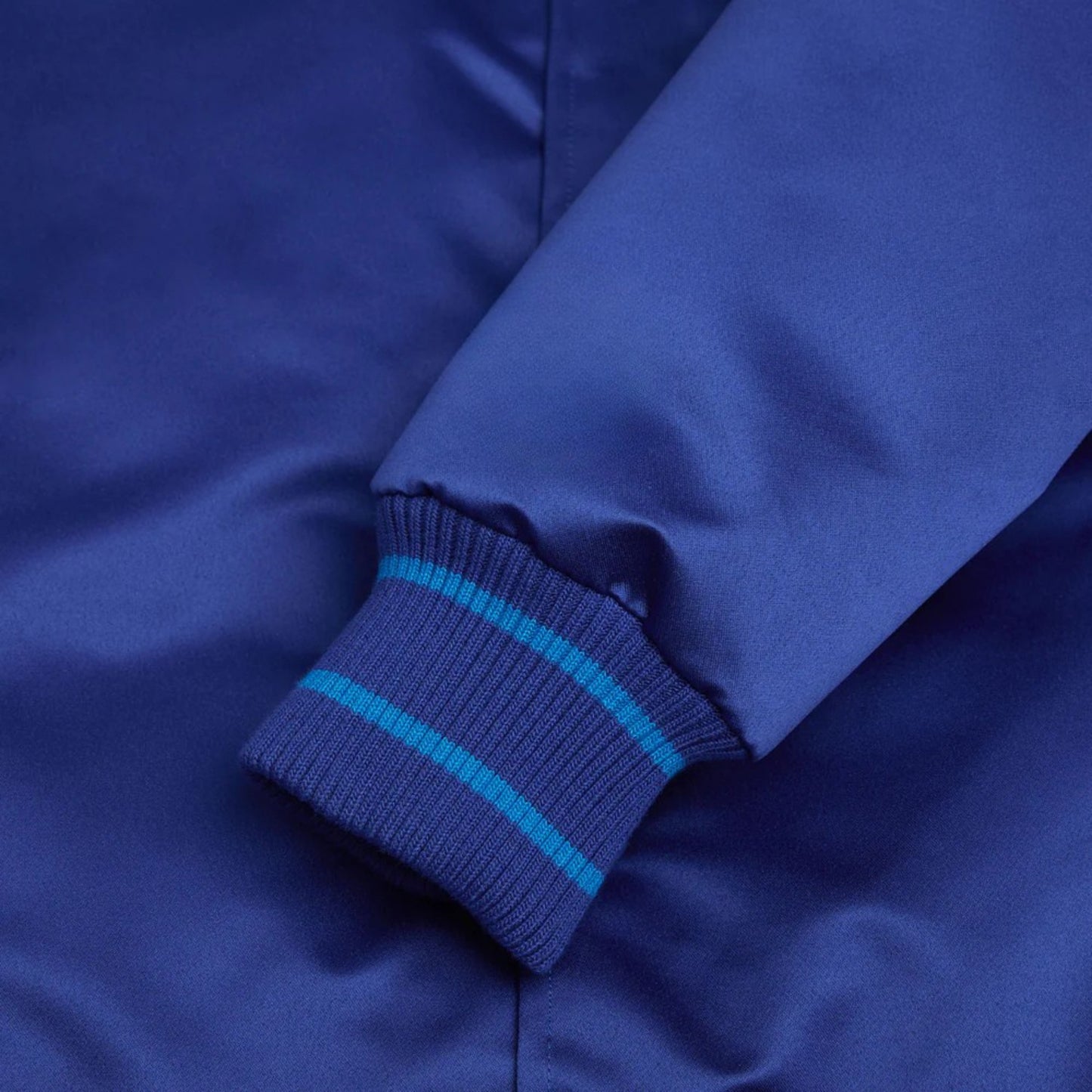 Close-up of a blue jacket with a ribbed sleeve and blue stripes.