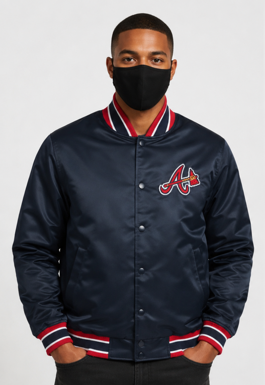 A man wearing a navy blue satin baseball jacket with a red and white striped ribbed collar, cuffs, and hem, featuring the Atlanta Braves 'A' logo on the chest. He is wearing a black face mask and standing against a light gray background.