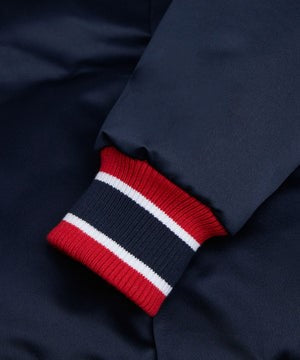 Close-up of a navy blue garment cuff with a ribbed knit trim featuring red and white stripes.
