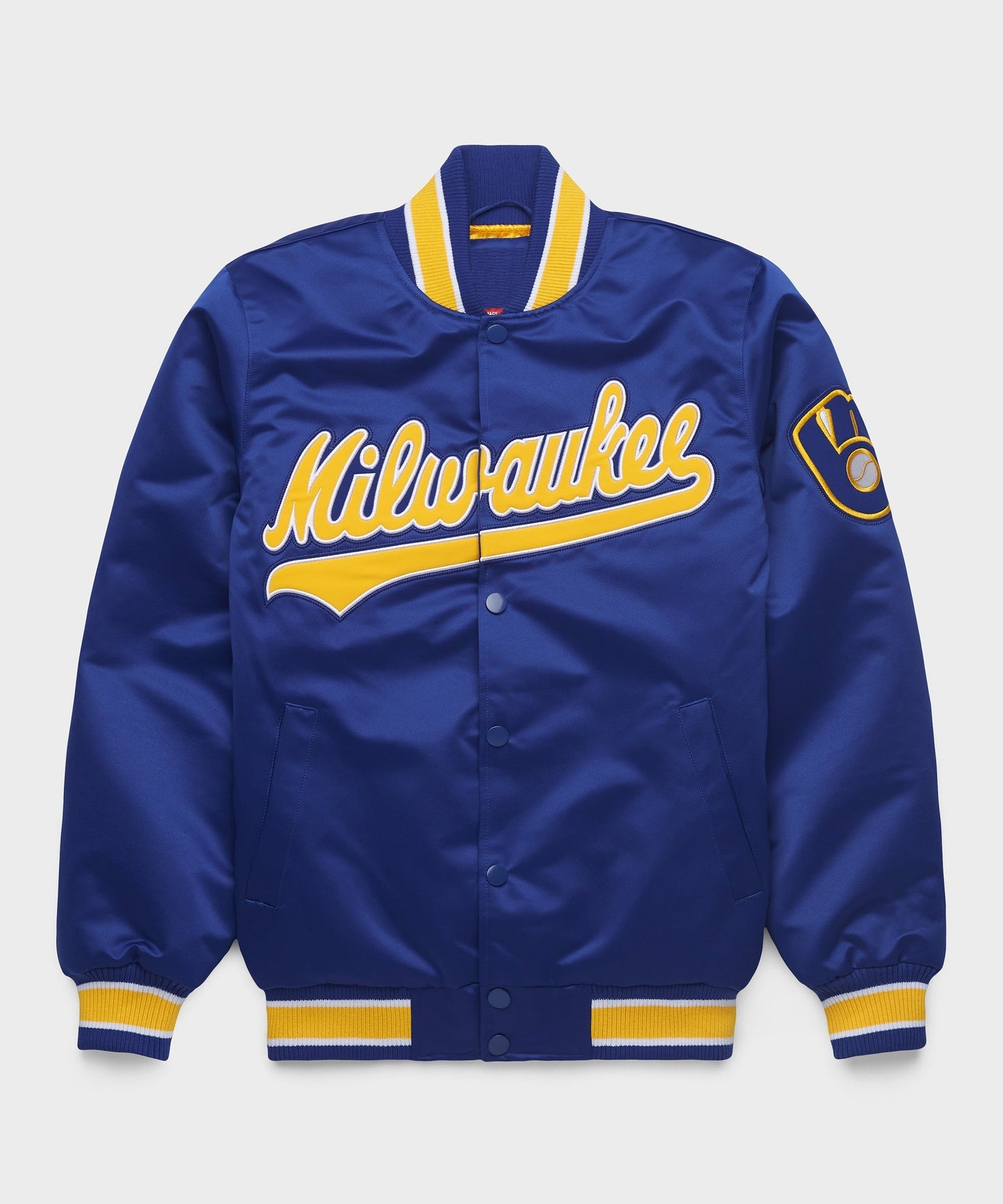 A royal blue satin varsity jacket with yellow and white trim, featuring 'Milwaukee' in yellow script across the chest and a circular patch on the left sleeve, shown against a light gray background.