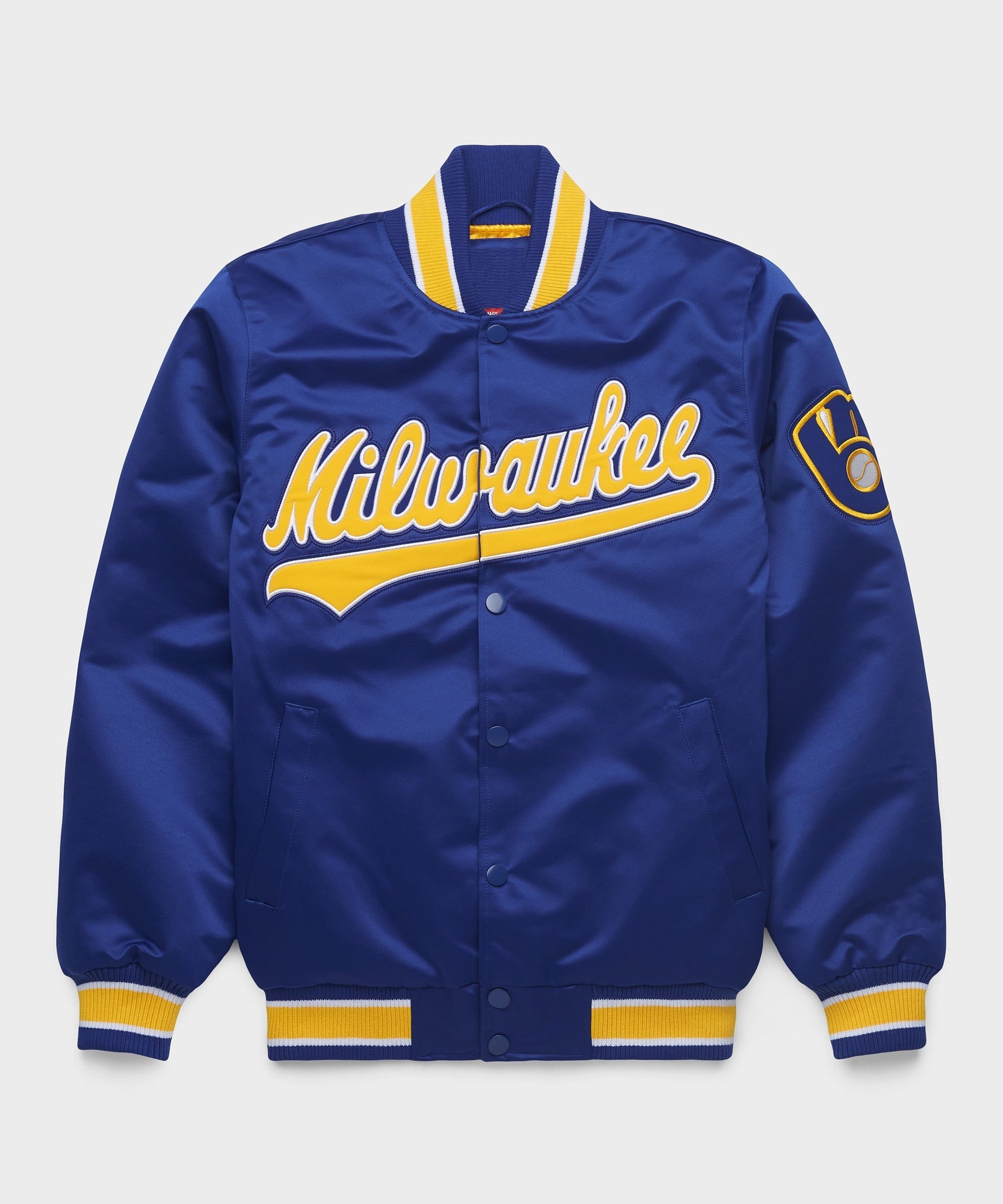 A royal blue satin varsity jacket with yellow and white trim, featuring 'Milwaukee' in yellow script across the chest and a circular patch on the left sleeve, shown against a light gray background.