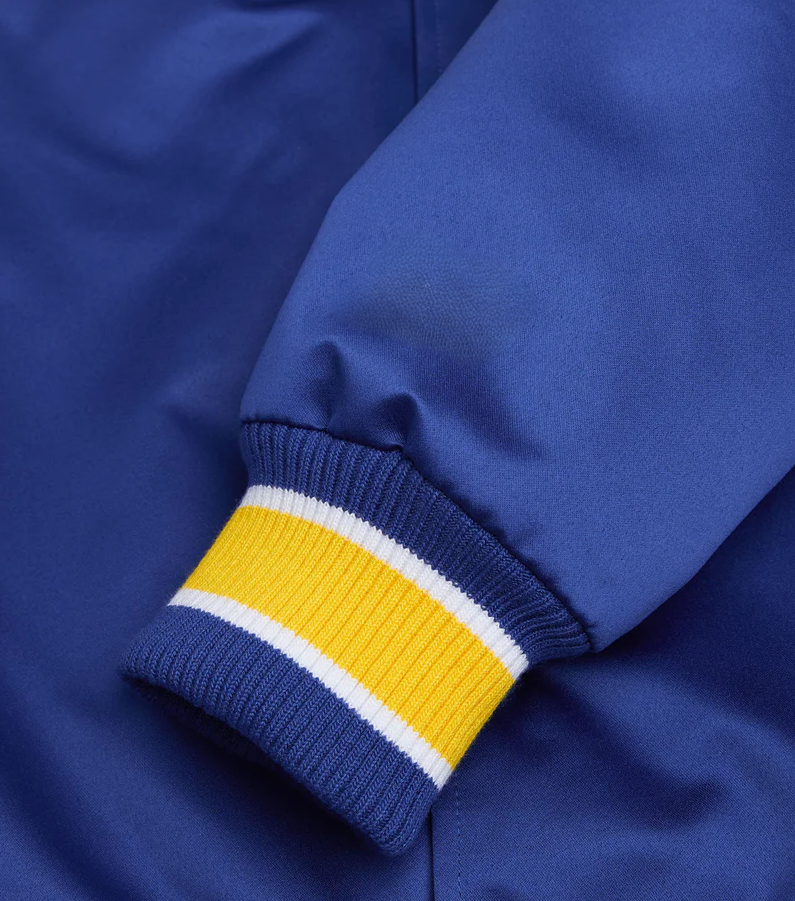 Close-up of a blue satin jacket sleeve with a ribbed cuff featuring yellow and white stripes.