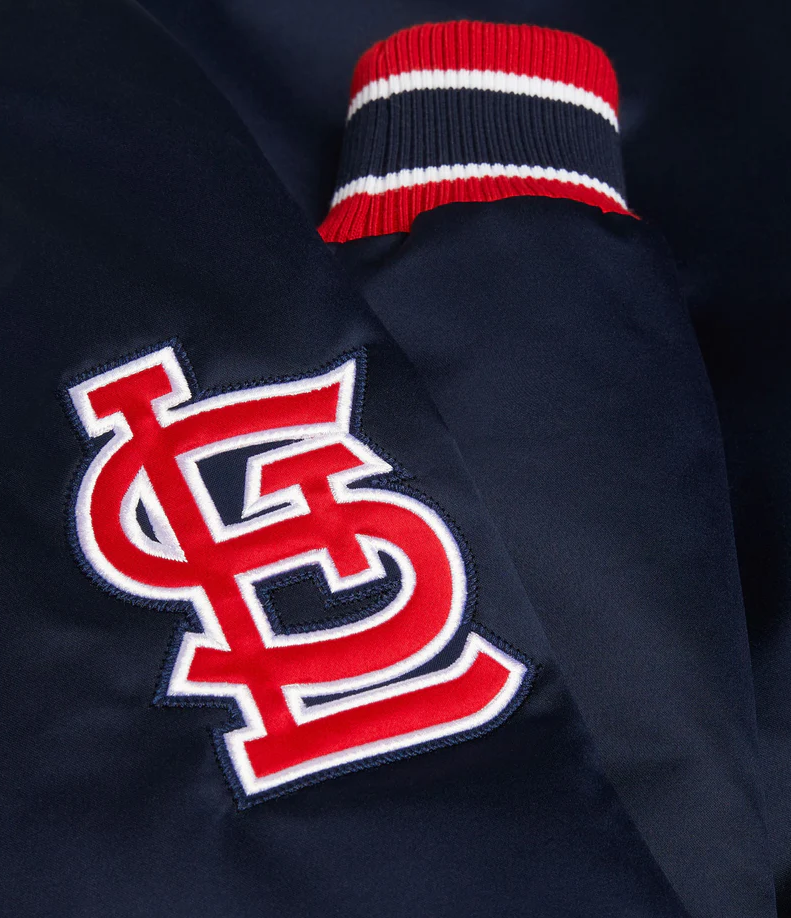 Close-up of a navy blue jacket or sweater featuring a large red and white embroidered St. Louis Cardinals 'SL' logo on the chest and a red, navy, and white striped ribbed knit collar.