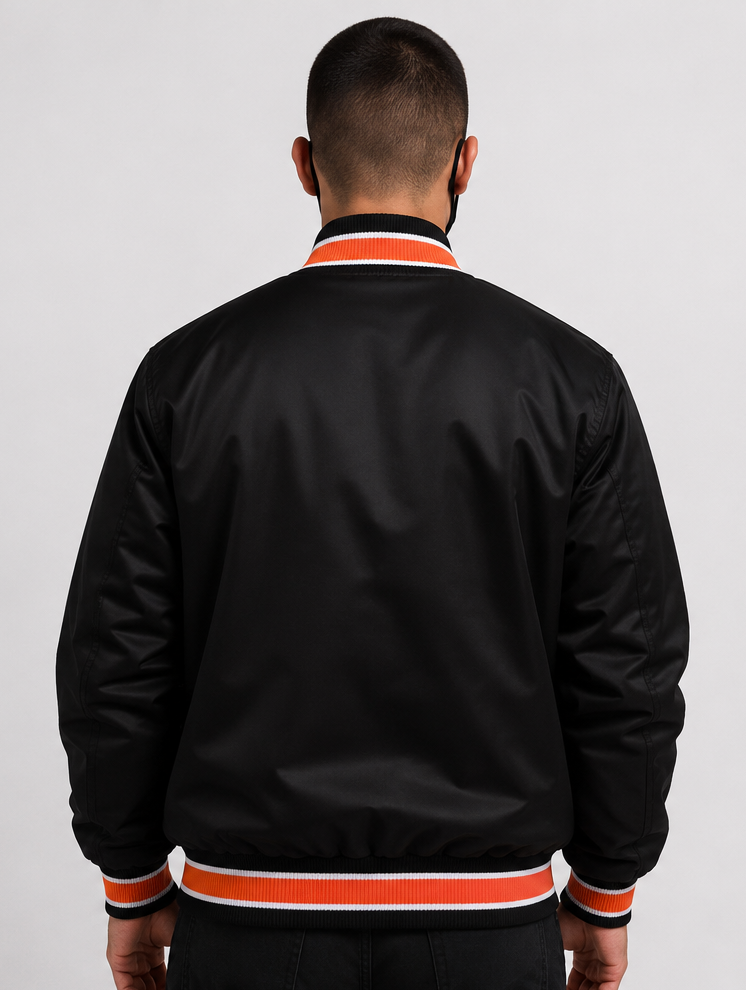 A man viewed from behind wearing a dark brown satin bomber jacket with orange and white ribbed trim on the collar, cuffs, and hem, against a light gray studio background.