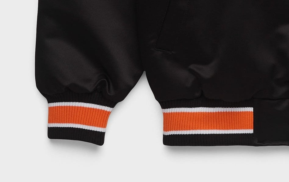 Close-up of dark brown satin-like pants or jacket legs with ribbed cuffs featuring orange and white stripes, shown on a light gray background.