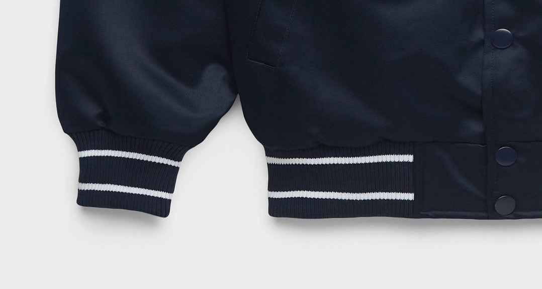 Close-up of a navy blue jacket sleeve with ribbed cuffs featuring two white stripes, set against a light gray background.