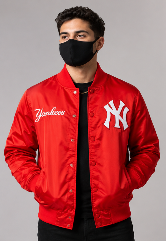 A man wearing a bright red New York Yankees satin bomber jacket with white embroidered logos, a black face mask, and a black t-shirt, photographed against a neutral gray studio background.