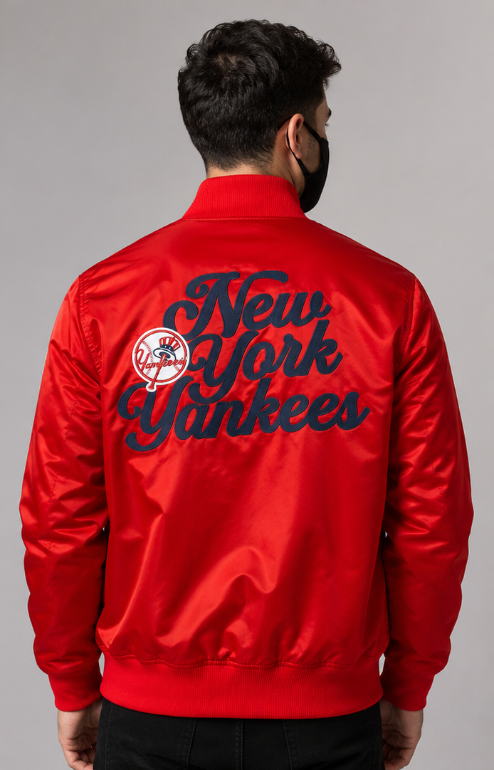 A man viewed from the back wearing a bright red satin bomber jacket with large navy 'New York Yankees' script and a team logo on the back, against a plain gray studio background.