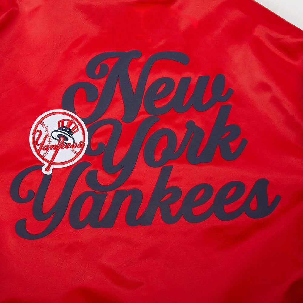 Close-up of a red fabric item featuring large navy script reading 'New York Yankees' with a circular Yankees logo patch on the left side.