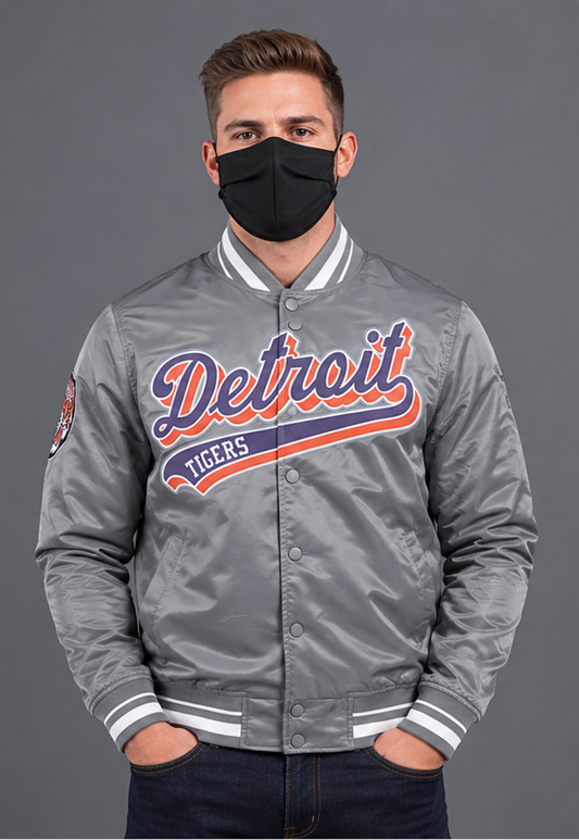 A man wearing a gray satin Detroit Tigers varsity jacket with a black face mask, standing against a solid gray studio background.